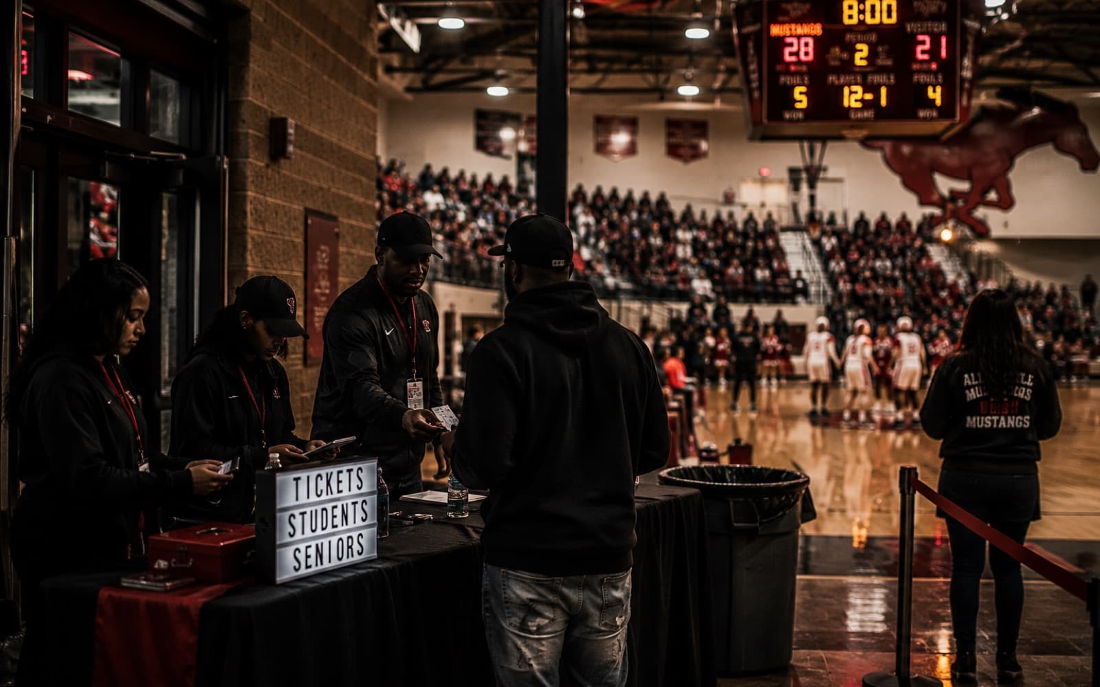 A game-night entrance: gate crew at the ticket table with packed bleachers behind